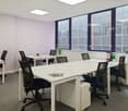 Modern office space with white desks, black office chairs, large windows, and a small refrigerator/dishwasher unit.