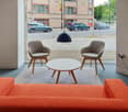 View of street, large windows, grey chairs, round table, large orange couch, glass wall