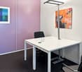 A room with a desk, three chairs, wall with art, pink wall, white table, light fixture