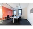 Modern office space with large windows providing a view, white walls, black office chairs, and a long conference table with chairs.