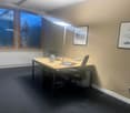 an office room with a desk, two chairs, lamp, picture frames, power outlets, a radiator and windows