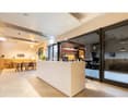 A modern office space with large windows, glass doors, hardwood floors, white walls, large desk, tables, and chairs.