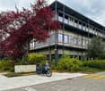 multistory building, grey and black facade, trees, bushes, grey pavement, motorcycle