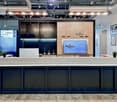 Reception desk with counter, modern style, wooden cabinets, large monitor with company logo, plants, large open room with glass walls