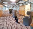 Long hallway with beige carpeting, glass doors, round ceiling lamps, tables, round chairs, lamps, potted plants