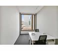 white walls, gray carpet, large window, white desks, black chairs, power outlet, large view of a city outside