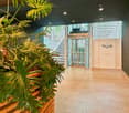 Open foyer, glass elevator, and stairs, indoor plants, gray walls, glass doors with Regus text, and glass windows with blinds