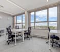 modern office with white tables and black chairs, large windows with blinds, ceiling lights, grey carpet