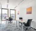 white walls, gray carpet, 2 white tables, black chairs, office doors, office desks, windows, artwork on walls