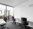 modern office with white walls, large windows, white desks, black chairs, carpeted floor