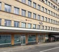 Large building with many windows, two signs on the front, one saying 'Regus' and the other 'OSO VAUD', a person walking on the sidewalk, a car parked in front of the building