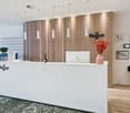 white reception desk, wooden wall, hanging lamps, monitor, vase with flowers, potted plant, trash bin