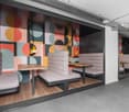 Modern and colorful office or cafe space with geometric wall mural, gray upholstered seating, wooden tables, and pendant lighting fixtures.