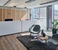 Reception area with wooden desk, two chairs, table with books, plants, and a monitor