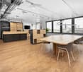 modern office room with wooden floor, large windows, wooden desk, chairs, cabinets, monitor, and plants