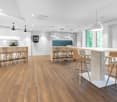 modern kitchen with wooden floor, white walls, large white table, wooden chairs, cabinets, ceiling lamps, windows