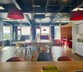 Open office space with large windows, red pendant lamps, wooden table and chairs, kitchen area with appliances