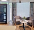 modern office room with wooden floor, two armchairs, round table, glass doors, plants, and a small office booth