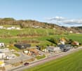 Aerial view of a residential area with several houses, green fields, and a road.