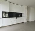 Modern, open-concept kitchen with white cabinets, black countertops, built-in oven and dishwasher, and tile flooring