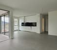 Open-concept living space with large windows, sliding glass doors leading to a balcony, modern white kitchen with black countertops, and tiled flooring throughout.