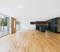 Spacious open-concept living area with hardwood flooring, large windows, and sliding glass doors leading to a balcony or terrace. The kitchen features modern green cabinets and appliances.