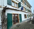 3-story white building with green shutters, a signboard, and vines growing around the front entrance