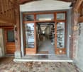 Wooden entrance, tiled walkway, storefront glass doors, interior shelves with items