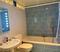 blue tiles, mirror with lighting, sink, toilet, bathtub with shower, blue curtain