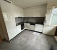 modern kitchen with white cabinets, black countertops, gray tiles, dishwasher, washing machine, sink, faucet, window