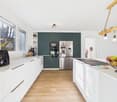 modern kitchen with white cabinets, wooden floor, green cabinets, stainless steel appliances, large window