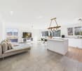 Open-plan living and dining area with large windows, modern kitchen, comfortable sofa, TV, dining table, chandelier, wooden floor