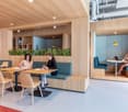 Modern open office space with wooden walls, desks, seating, plants, and lamps