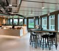 open space office with a reception area, desk, counter, stools, modern lighting, plants, windows with a city view
