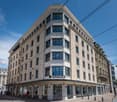 6-story building with modern architecture, large windows, storefronts, bollards on street side, street signage