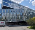 Modern office building, large glass windows, 'SPACES' sign, elevated ground level, surrounding trees and street