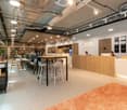 modern office space, reception desk, seating area with tables and chairs, wooden flooring, glass walls, ceiling lights, shelves with books and plants