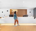 Reception desk, wooden paneling, monitor, staff member, wooden flooring, open space, ceiling lights