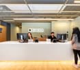 Modern office space with a reception desk, computers, and employees working. The space has a clean and minimalist design with wooden accents and a large 'SPACES' logo on the wall.