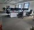 modern office with desk and office chairs, 6 computer screens, carpeted floor, natural light from windows