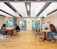 Open area, oval wooden table with chairs, round benches along wall, ceiling lamps, windows, lamps on tables, wooden floor
