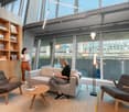Spacious and open interior with large glass windows, couch, chairs, and table. There is a bookshelf filled with books and decorative items.