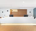 modern office reception, white front desk, wooden wall, LED lighting, minimalist decor, clean and organized