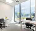 Bright and modern office space with large windows overlooking a landscaped outdoor area. The room has a desk, chairs, and a small storage unit. The space appears to be well-lit and designed for professional use.
