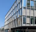 Modern office building with glass walls and many windows, 5 stories, silver frame around windows, corner building