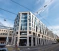 4 story office building, modern design, large glass windows, arched entrance, street level shops, tramway tracks