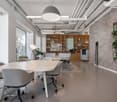 Open concept office space with white walls, exposed ceiling, large windows, wooden shelving unit, conference table with chairs, and a plant decoration.