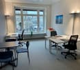 modern office room with large windows, white walls, white desks, black chairs, radiator, floor lamp, picture on wall, plants