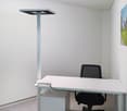 Modern office with white walls, desk, black office chair, standing lamp, storage cabinet, painting on the wall.