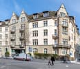 Large multi-story building, stone exterior, multiple balconies with railings, several windows